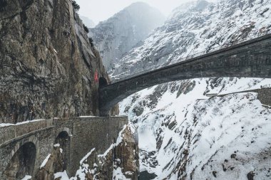 Kırsal bölgedeki kayalık, eski bir köprünün manzarası karlı dağlarla çevrili.