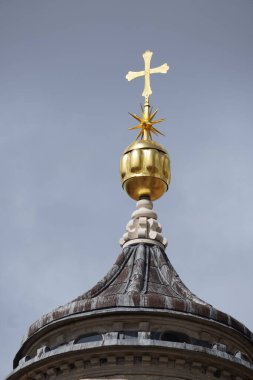 Bir kilisenin altın haçının dikey görüntüsü gri gökyüzünün arka planına karşı.
