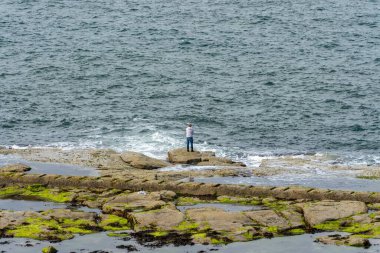 Whitley Bay, İngiltere 'de deniz balıkçılığı yaparken bir adam bir kayanın üzerinde duruyor..