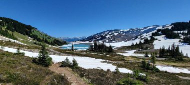 Güneşli bir günde dağlarla çevrili güzel bir göl manzarası.