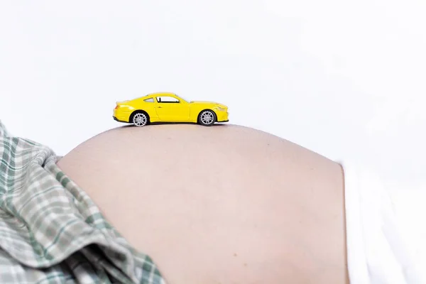 白い背景を持つ妊娠中の腹に黄色のおもちゃの車の閉鎖 — ストック写真