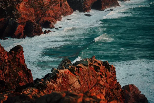 Atlantik okyanus dalgalarının Lizbon yakınlarındaki Cabo da Roca 'daki kayalara vuruşunun manzarası, güneşli bir havada Portekiz