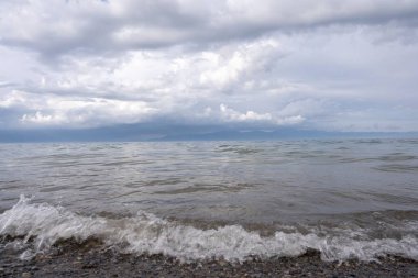 Okyanus dalgalarının bulutlu havada sahile vuruşunun manzarası.