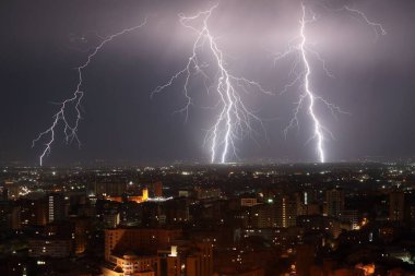 Gece gökyüzünde bir şehrin üzerine düşen güzel bir yıldırım.