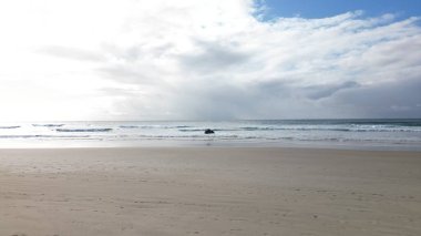 Bulutlu bir gökyüzünün altında boş manzaralı bir plaj