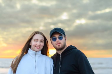 Gün batımında deniz kenarında poz veren mutlu beyaz bir çift.