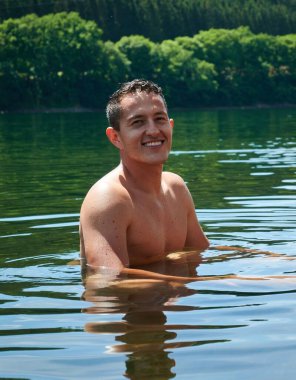 Gölde gülümseyen bir adamın ormana bakan kameraya baktığı dikey bir görüntü.