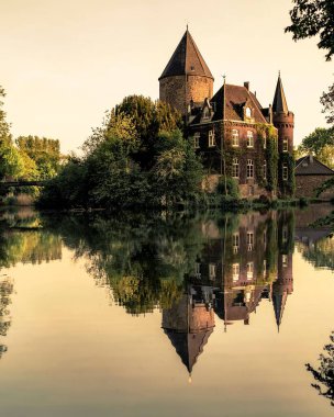 Gün batımında gölde yansıması olan eski bir kale.