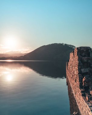 Güneşin altında, sakin bir gölün yanında taş bir duvar.