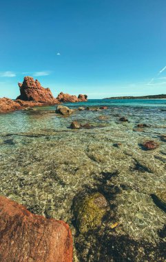 Güneşli bir günde kayalık bir sahilin turkuaz bir denize karşı dikey çekimi.