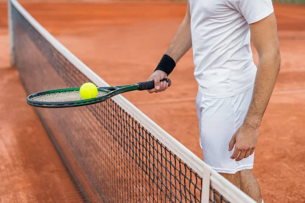 汚いテニスコートのネットの近くにボールでラケットを持っている若い男 — ストック写真