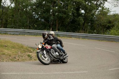 Güneşli bir günde kırmızı bir Honda CB750 bisiklet süren iki kişi.