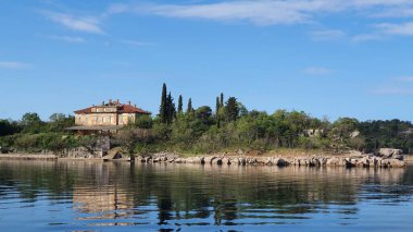 Yeşil ağaçları ve evi olan güneşli bir sahil.