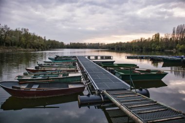 Güneşin battığı bulutlu bir günde rıhtımda demirlemiş teknelerin manzarası.
