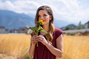 Sıradan giyimli genç kadın tarlanın önündeki ayçiçeğini kokluyor.