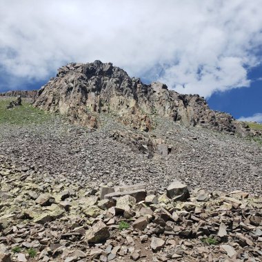 Güneşli bir günde bulutlu gökyüzünün altında kayalık yamaçların ve dağın tepesinin manzarası.