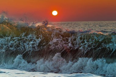 Güzel bir gün batımı manzarası. Güçlü ve büyük deniz dalgaları üzerinde turuncu ve kırmızı bir gökyüzü.
