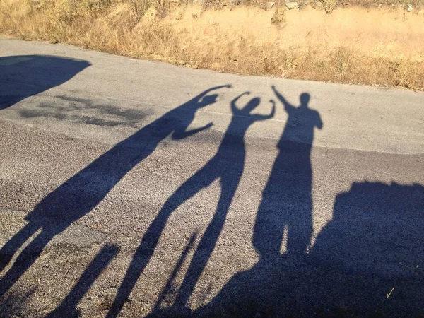 道路上で空気中の彼らの腕で異なるポーズの3人の長い影 — ストック写真
