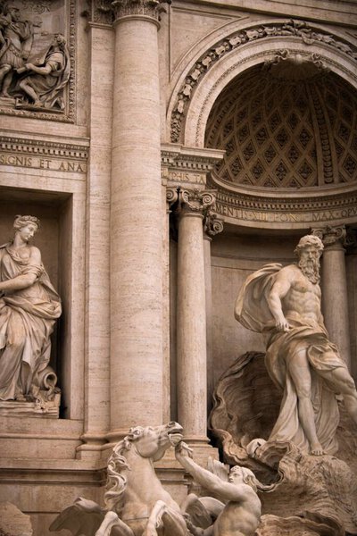 A vertical shot of a antique architectural building with marble statues with columns and an arch