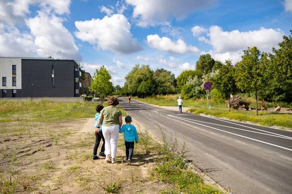 アスファルトの道路と緑の木々の隣を歩いている女性と2人の子供は ベルナータ通りの新しいアパートの建物につながります — ストック写真