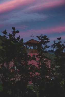 Çatıda pembe ve tutkal gün batımına karşı çapraz bir kulenin dikey görüntüsü.