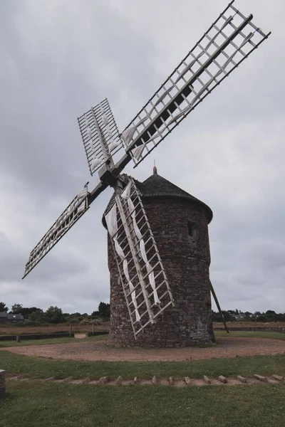 A vertical shot of a old big windmill with a gloomy sky on the horizon