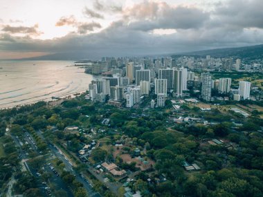 Oahu, Hawaii 'nin yeşil sahillerindeki Honolulu' daki binaların günbatımında mavi denize bakan hava manzarası.