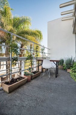 Sandalyeleri, masası ve bitkileri olan çitlerle çevrili bir balkonun dikey görüntüsü.