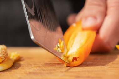 Kırmızı biberin çekirdeklerini bıçakla soyan bir adamın elini yakından çek.