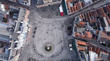 Küçük evler ve binalardan oluşan eski mimari yapılara sahip bir şehirde çeşmeli bir meydan manzarası.