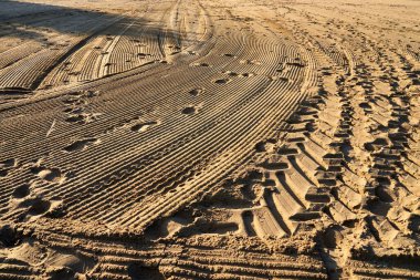 Lastik izleri ve ayak izleri olan kumlu kahverengi bir yüzeye yakın çekim.