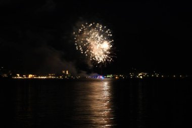 Gece gökyüzünde parlayan ve Tegernsee, Bavyera, Almanya 'da suyu yansıtan güzel altın havai fişekler.