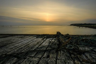 Ahşap yüzey üzerinde ipler ve algler olan bir limandan çekilen alçak manzara, gün batımı.