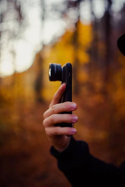 Sebuah Tangan Memegang Telepon Dengan Lensa Kamera Hutan Musim Gugur — Stok Foto
