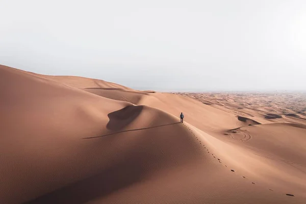 青空の下砂漠の風景の中に一人で砂丘を歩く男 — ストック写真