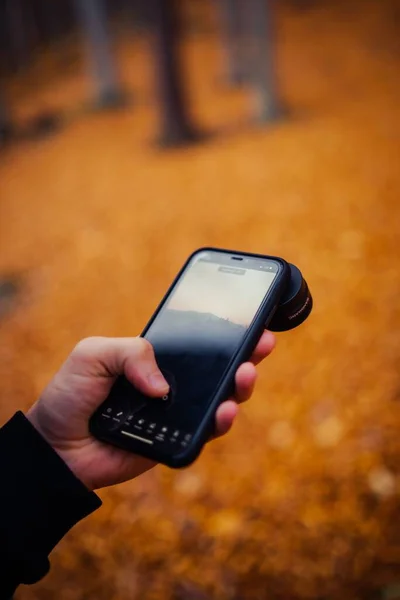 秋の森の中でカメラレンズを持った携帯電話を手に — ストック写真
