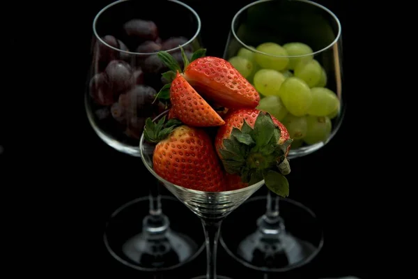 在黑色背景上隔离的透明玻璃杯中的草莓和葡萄特写镜头 — 图库照片