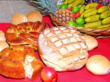 Muz, ananas, limon, üzüm ve çilekli hasır sepet. Çeşit çeşit ekmekler, kırmızı jüt ile süslenmiş bir masada pasta..