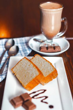 Dikey bir cappuccino ve masada dilimlenmiş tatlı.