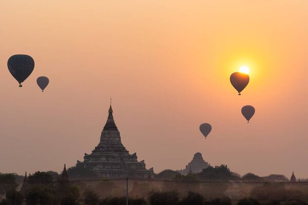 A silhouette of the Shwesandaw Phaya Pagoda in Bagan, Myanmar, with air balloons at sunrise