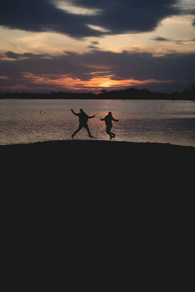 Vertical Shot Silhouettes People Jumping Shore Dark Sunset Sky — Stock Photo, Image
