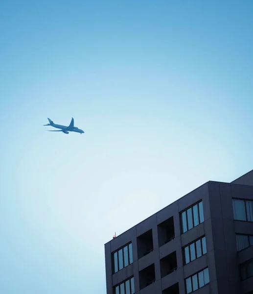 灰色の近代的な建物の上を飛ぶ飛行機の垂直方向の眺め — ストック写真