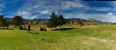 Arka planda iki golf arabası olan bir adamın panoramik görüntüsü.
