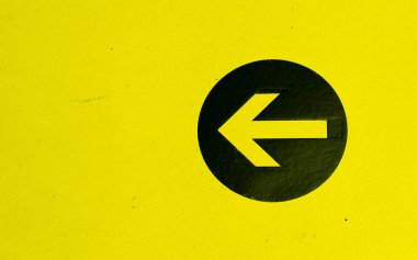 Sarı bir duvara izole edilmiş siyah bir çemberin üzerindeki bir ok yönü gösteriyor.