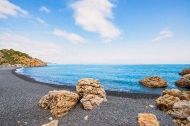 Chios Yunanistan 'da siyah çakıl taşlı Mavra Voila plajı. Büyük kayalar ve güzel bir su manzarası var.