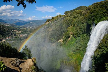 Vadinin üstündeki gökkuşağı mavi gökyüzünün altındaki şelalenin yanında.