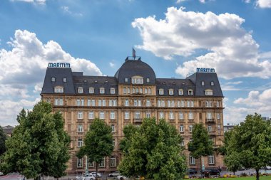 Mannheim 'daki Maritim Oteli. Mavi gökyüzünün altında bulutlu ağaçların arkasında.