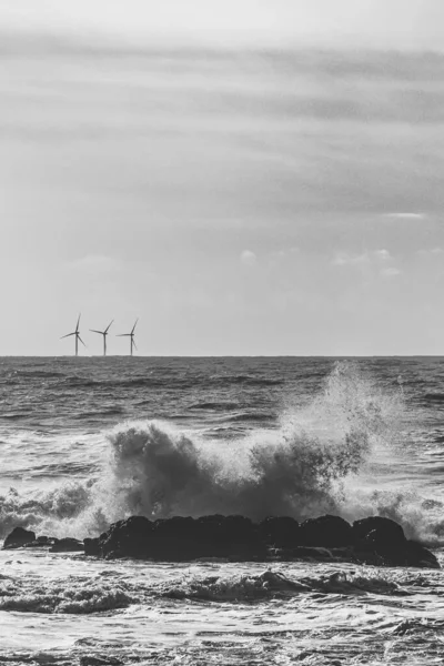 背景に風力タービンと海の波の垂直グレースケールショット — ストック写真