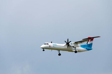 Gökyüzünde mavi bulutlarla uçan beyaz bir uçak.