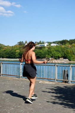 Dikey çekimde genç bir kadın spor giysiler giyiyor ve ip atlıyor.